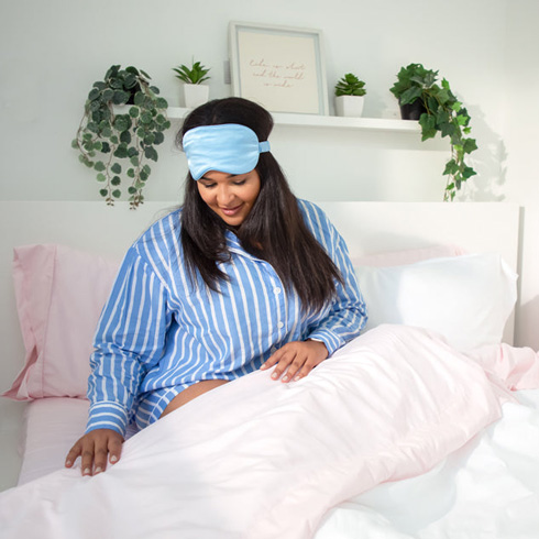 Woman wearing blue pajamas in a bed with white and pink sheets.