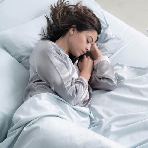 Woman with brown hair sleeping comfortably on blue sheets