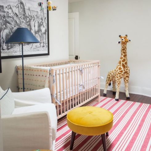 Nursery room with crib. large giraffe stuffie, striped red rug and yellow stool.
