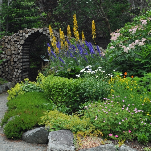 An archway made of stacked logs and flowers in the Pollinator Garden at the Memorial University Botanical Gardens
