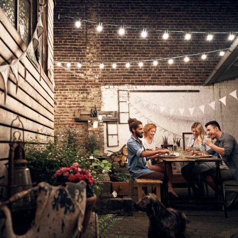Small backyard with string lights and friends eating dinner at table.