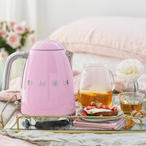 A retro-style pink Smeg electric kettle on. serving tray with breakfast dishes and tea