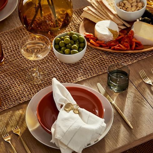 Beautiful Thanksgiving table décor featuring West Elm Botanical Napkin Rings that are stainless steel with a brass finish, red bowls, white chargers, gold tableware, a bowl of green olives and cheese plate