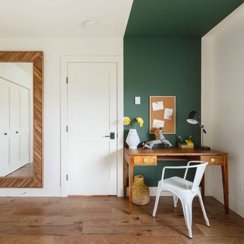 Home décor renovation designed by David Strongman of an office space with wide plank wood floors, a large wall mirror, white door, wooden desk, white desk chair, and a corkboard on a wall painted in emerald green as featured on HGTV Canada