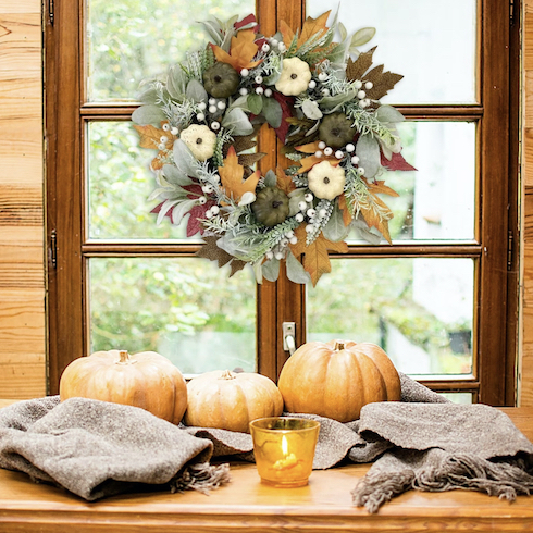 Gorgeous fall wreath with an eye-catching combination of fall elements of oak and maple leaves and swirls of berry clusters that hangs on a set of French doors behind a set Thanksgiving table