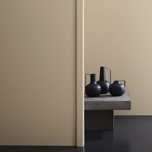 A wall painted in Benjamin Moore Bleeker Beige HC-80, a medium buff hue with pleasing gray undertones, with a bench holding three black vases