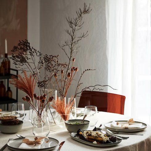 Beautiful Thanksgiving table setting by Ikea Canada with plates filled with food, vases with rust colours branches and grasses, and a rust coloured lucite chair