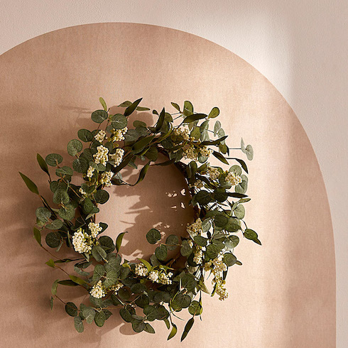 Simons Maison wreath made of eucalyptus branches adorned with berries hangs on a dusty rose wall