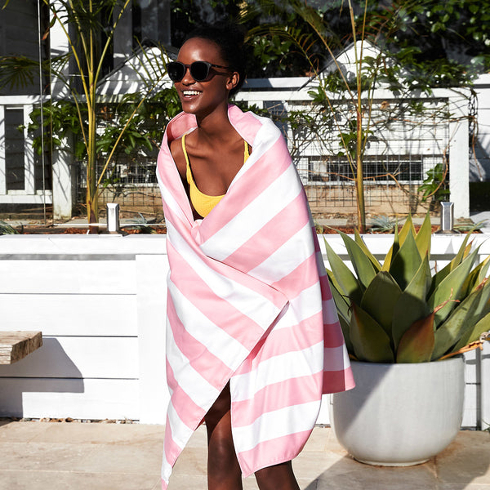 A woman wearing sunglasses and a yellow bikini drapes a white and pink beach towel over her shoulders