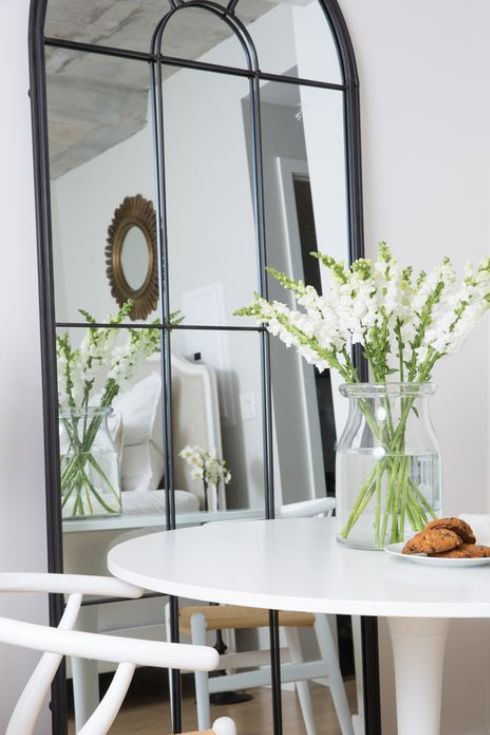 Large black paned mirror leaning against wall in kitchen bedside white table bistro set.