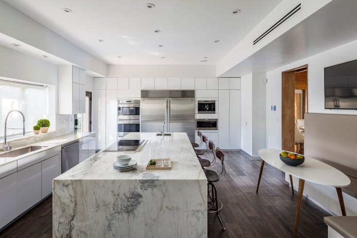 A modern chef's kitchen with marble counters and seating
