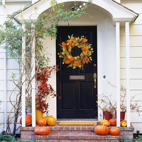 Gorgeous orange fall wreath on black door with pumpkins on doorsteps.