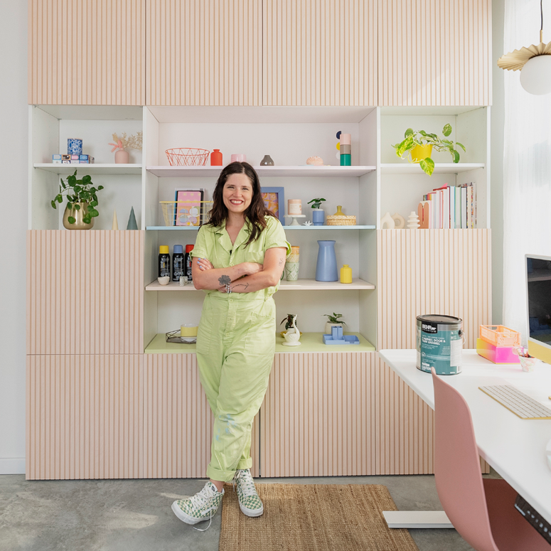 Maca Atencio standing in front of a colourful wall of cabinets and shelves.