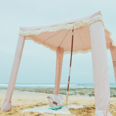 A shot of a large pink and white striped cabana with white tassels on the beach