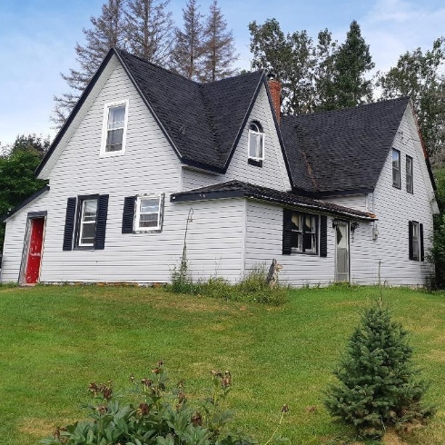 A large white farmhouse with white siding, red door and dark grey shingles