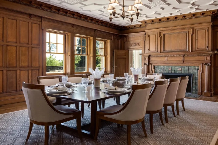A formal dining room with fireplace, large table with seating for 10, and wood-panelled walls