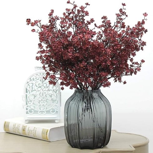 A smoky glass vase with deep burgundy fake flowers