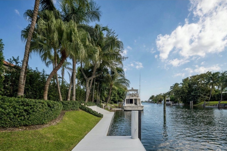 An extended boat dock with a yacht at anchor and large palm trees