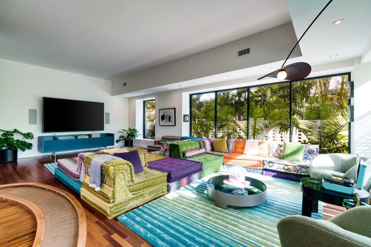 A living area with jewel-toned furnishings, floor-to-ceiling-windows and a large TV