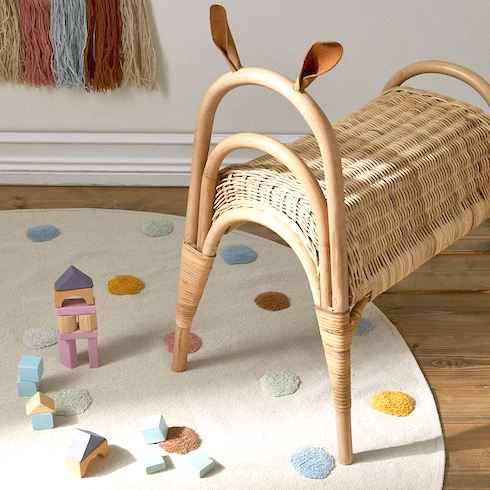 H&M Cotton Rug with Tufted Dots Round rug in woven cotton fabric with tufted dots in soft colours and on-slip protection at back sitting on a wooden floor in a nursery with a wicker animal bench, wooden blocks and woven wall hanging on the wall as featured in HGTV Canada's Best Nursery Rugs Under $200 Your Little One This Year