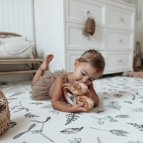 A toddler plays with a rattan rabbit toy while lying on her belly on a Little Bot Baby Ofie Plants + Eze Mat in a chic nursery play room with a white dresser and a low rattan bench seat as featured in HGTV Canada's Best Nursery Rugs Under $200 Your Little One This Year