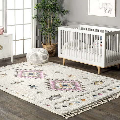 Polypropylene plush cozy shag rug laying in a chic nursery with grey wood floors, a white cotton pouf, a white wooden crib and a potted plant in a basket in the corner beside a set of French doors as featured in HGTV Canada's Best Nursery Rugs Under $200 Your Little One This Year