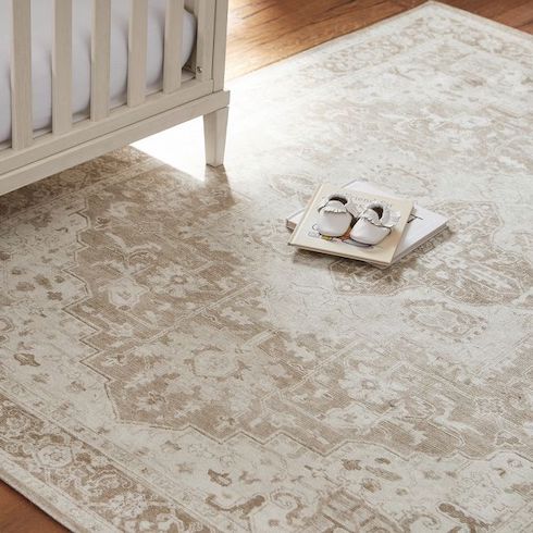 Ellington Washable Rug by Pottery Barn Kids sits on the wooden floor of a child’s nursery with a white crib, two books and pair of white leather baby slippers sitting on it as featured in HGTV Canada's Best Nursery Rugs Under $200 Your Little One This Year