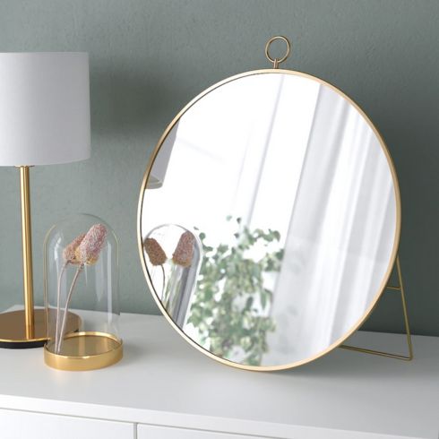 Small rounded mirror with gold frame on white dresser.