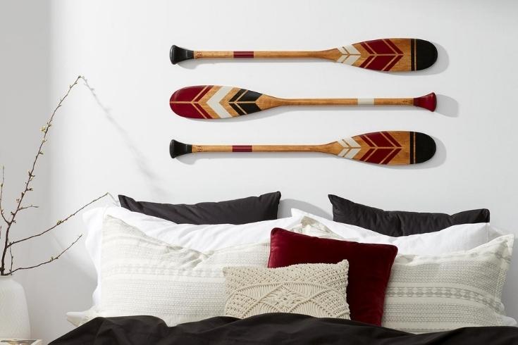 three wooden paddles on a white wall above a bed