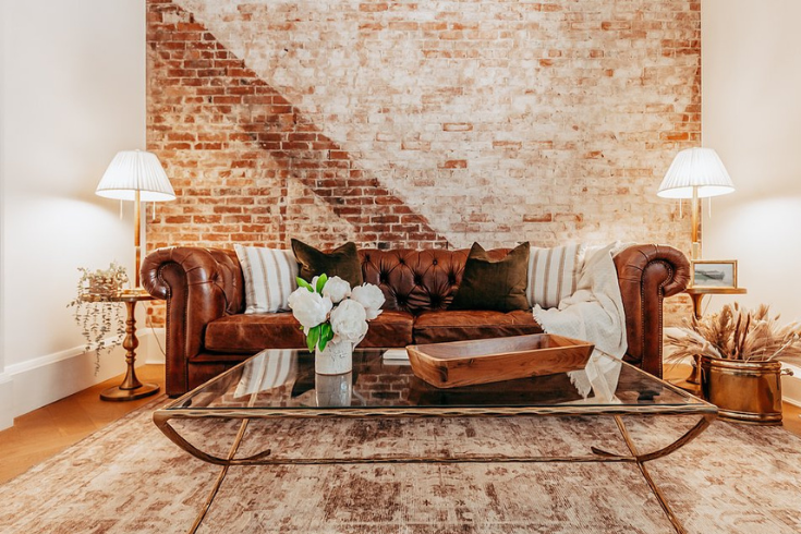 Living space with ustic exposed brick wall behind a leather couch and a glass coffee table