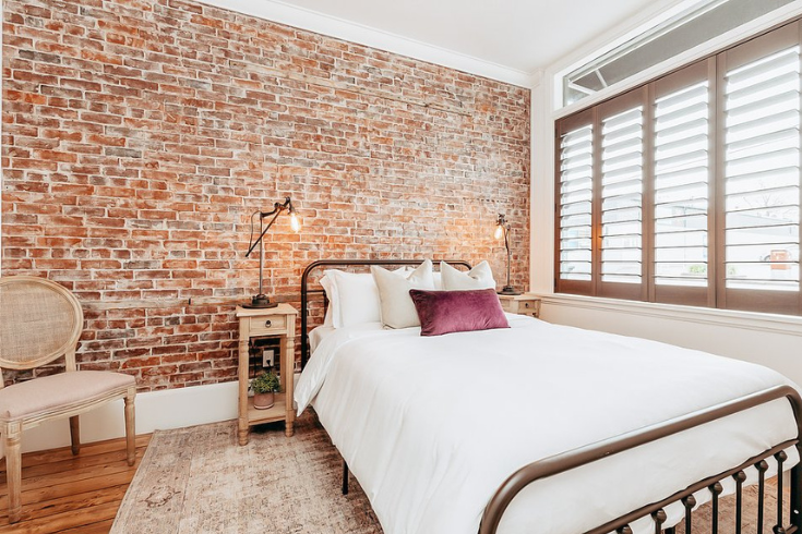 Secondary bedroom with a rustic exposed brick wall behind an industrial style bedframe 
