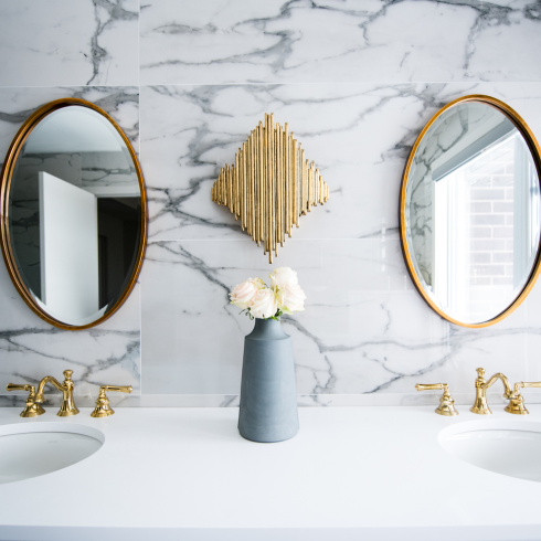 Modern bathroom double vanity with marble-look walls and oval mirrors.
