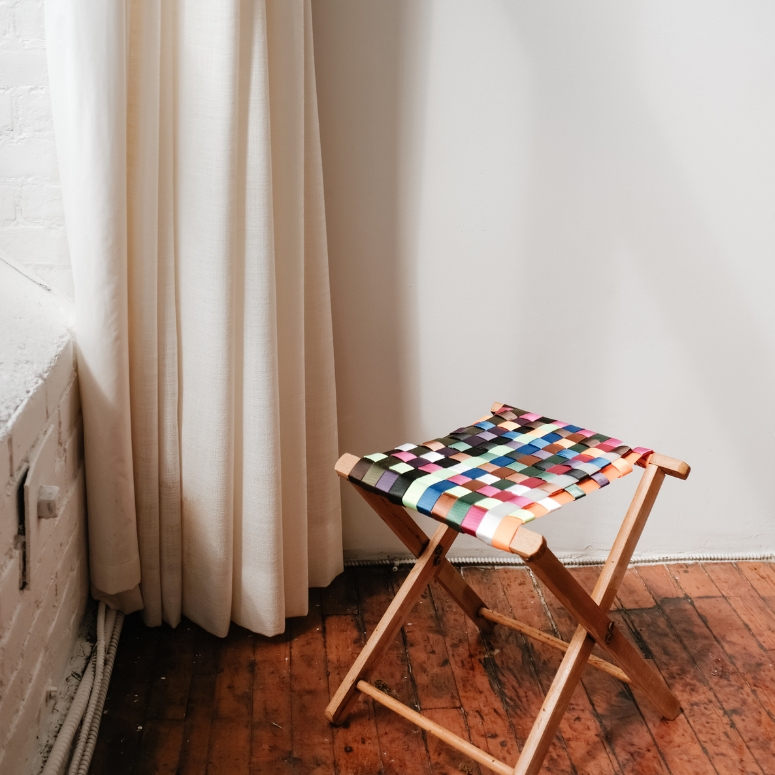 Colourful stool next to a beige curtain and window