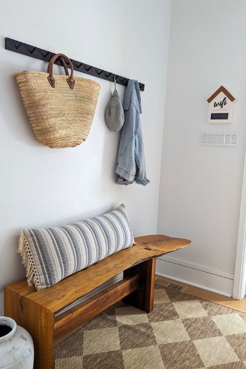 Organized mudroom/entryway with wood bench, wall hooks and beige patterned rug.