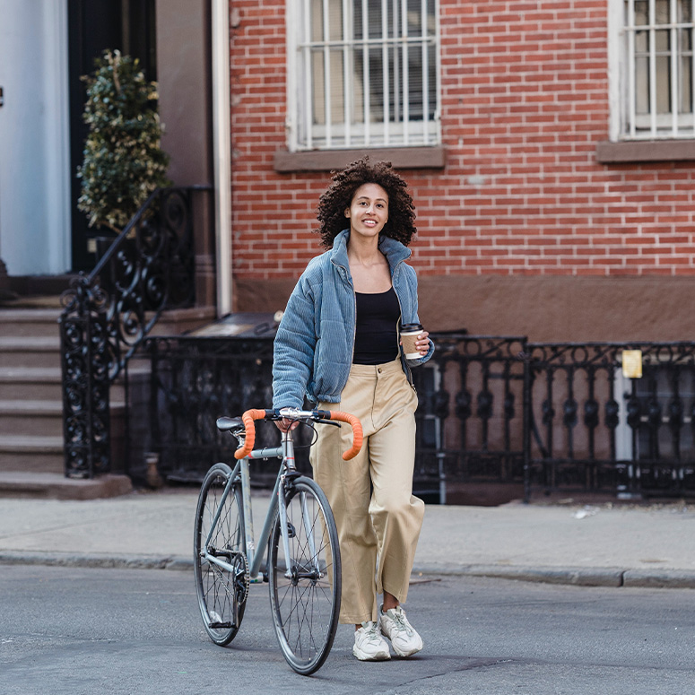 Woman walking with her bike and coffee in her hand