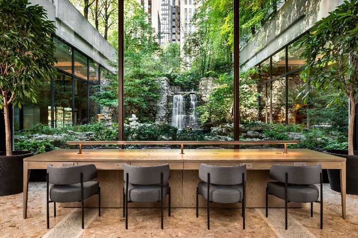 A hotel seating area with chairs, long table and a view of the couryard waterfall and greenery.
