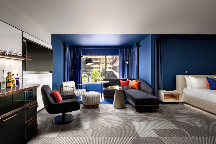 A hotel room with blue accent wall and large window, blue drapery