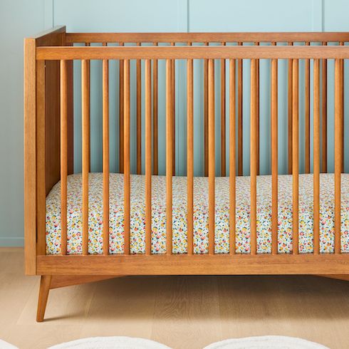 A wooden, mid-century modern crib with Misha & Puff Brimfield Floral Crib Fitted Sheet made in collaboration with West Elm
