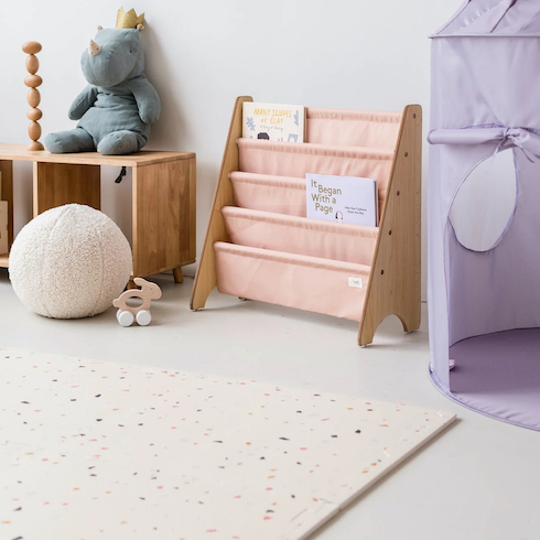 Terrazzo Palest Pink EVA Foam Play Mat from 3 Sprouts set up the floor in a small nursery along with a white spherical pouf, a pink baby bookshelf, a purple play tent, a blue stuffed rhino sitting on a wood credenza and a small wooden bunny toy on wheels