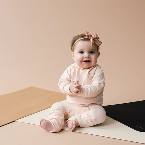 A set of three Bek & Jek Vegan Leather Changing Mats sit on the floor with a baby sitting happily on top of them
