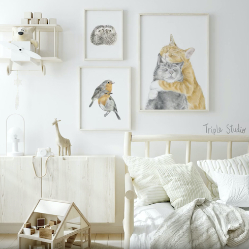 Sweet small white nursery or kids’ room with three watercolour animal prints by Triple Studio on a white wall along with a wooden airplane shelf, a floating white oak cabinet with a few toys on top, a wooden playhouse on the wooden floor, and cozy daybed piled with white pillows and throws