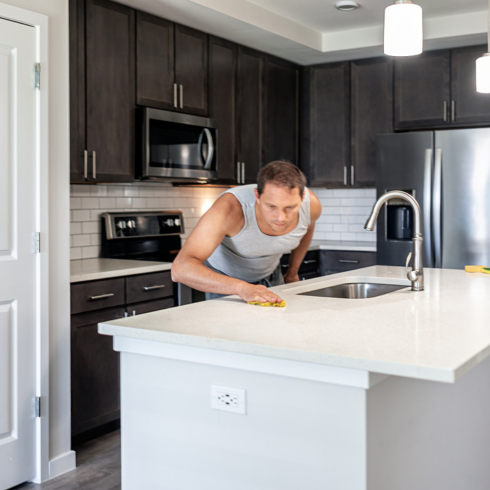 a young white man wiping down a marble kitchen island with a dry cloth
