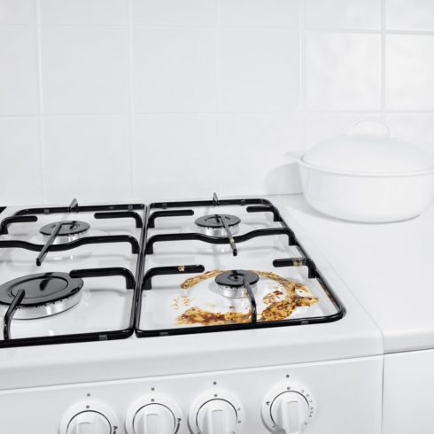 a dirty gas range burner in an otherwise pristine white kitchen