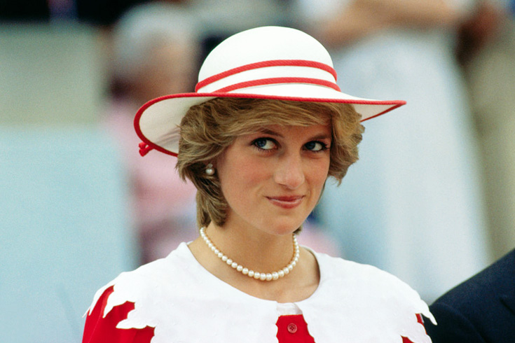 Princess Diana smiling subtly in a red and white hat with a wide brim. 