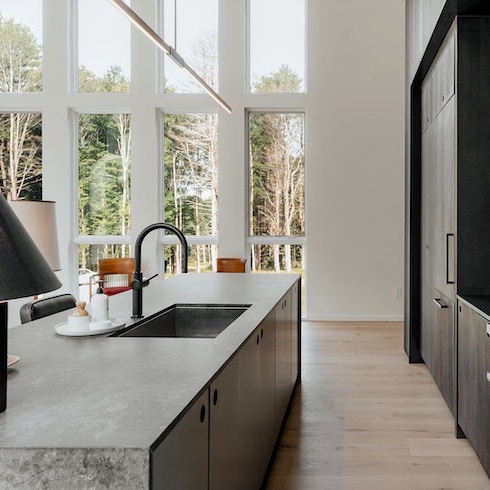 A bright kitchen with a concrete kitchen island and black cabinets