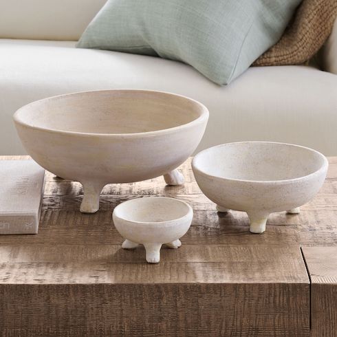 Gift idea - Three Artisan Rustic Handcrafted Ceramic Bowls by Pottery Barn sit on a wooden coffee table in front of a white couch with two pillows