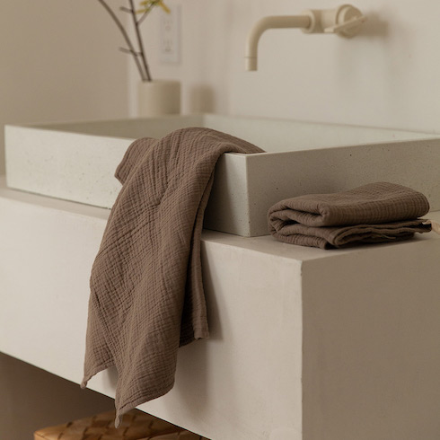 Gift idea - Les Écolorés sage green minimalist towels sold by Simons are draped on a white rectangular modern sink and folded on a white bathroom vanity beside the sink