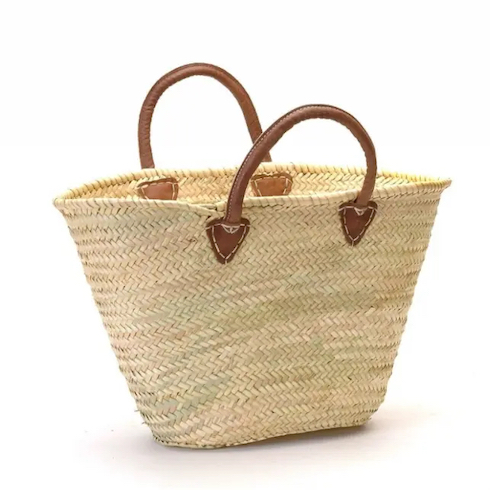 Gift idea - French Market Basket from Home Smith is a straw basket woven in tight chevron pattern and is accompanied by brown, buttery, short leather straps with thick white stitching shown against a white background