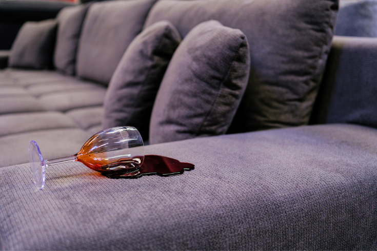 red wine spilling out of class on couch armrest 
