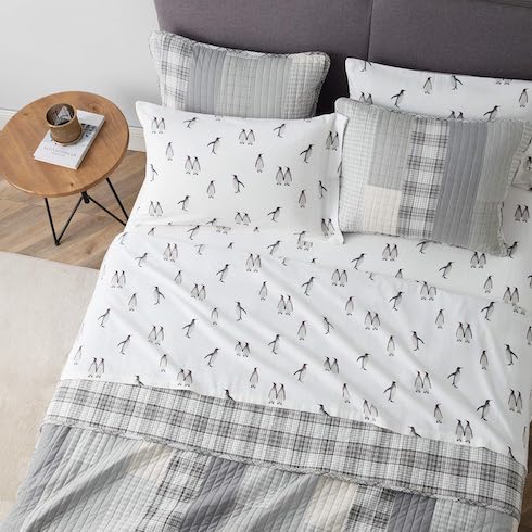 Eddie Bauer Rookeries Flannel Sheet set from Amazon.ca on a dark grey upholstered bed with a patchwork quilt comforter and four pillows, in a bedroom with wood floors, a cream coloured rug, and a wooden bedside table with hairpin legs and book and mug on top